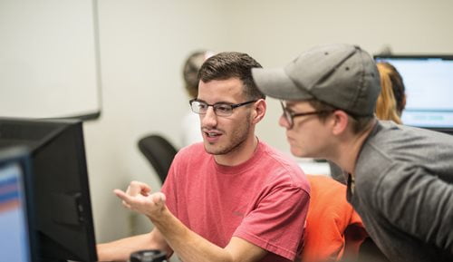 Student helping another student on a computer