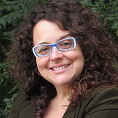 picture of Alicia Rueda-Acedo, dressed in a dark shirt with blue and white rimmed glasses