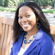 picture of Brandie Green, dressed in a blazer with matching earrings and necklace, sitting on a bench on campus