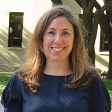 picture of Danielle Klein, dressed in a dark shirt with puffy sleeves in front of trees on campus