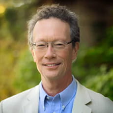 picture of David Hopman, dressed in a suit with glasses in front of bushes