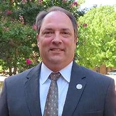 picture of Jerry Hubbard, dressed in a suit and tie in front of trees on campus