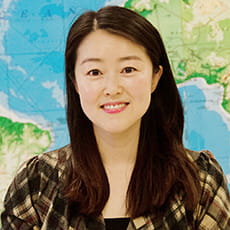 picture of Jiwon Suh, dressed in a checkered pattern shirt in front of a world map