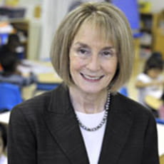 picture of Kathleen Tice, dressed in a blazer with a necklace on, posed in a children's classroom