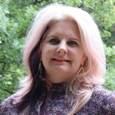 picture of Shelley Wigley, dressed in a floral shirt and dangling earrings in front of trees
