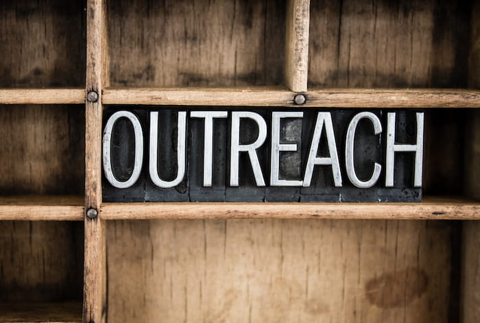 wooden sign with white letters that says outreach