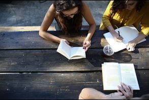 three students sitting outside at a table with journals and drinks