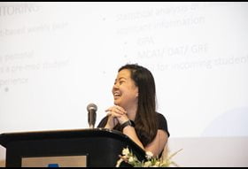 lady giving a presentation at a U T A event, her presentation displayed behind her