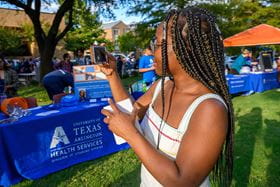 student taking a picture of one of the booths at a U T A tabling event on campus