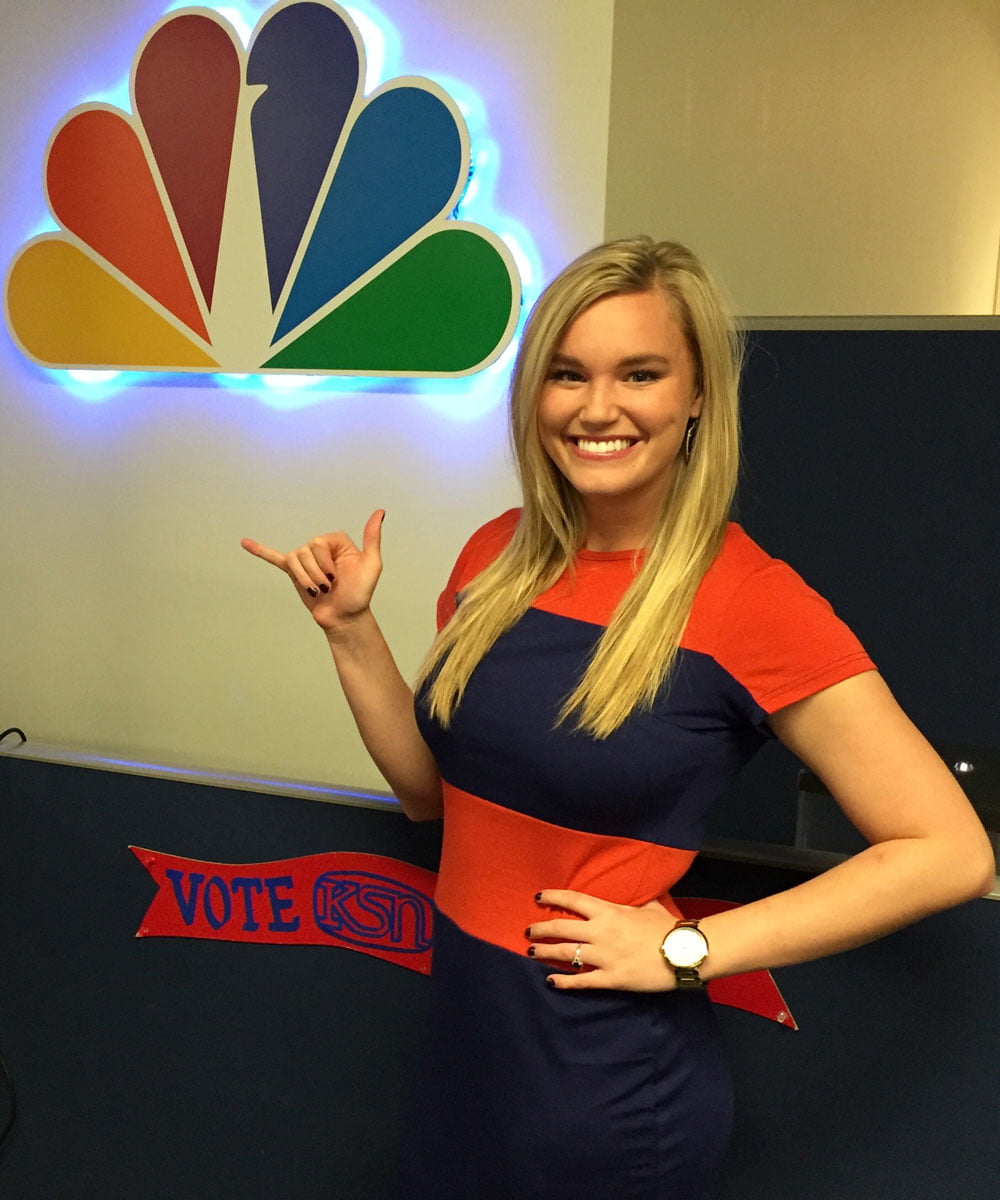 Avery Bottger in a striped blue and orange shirt holding the Mav Up hand sign in front of the NBC logo at their office." _languageinserted="true