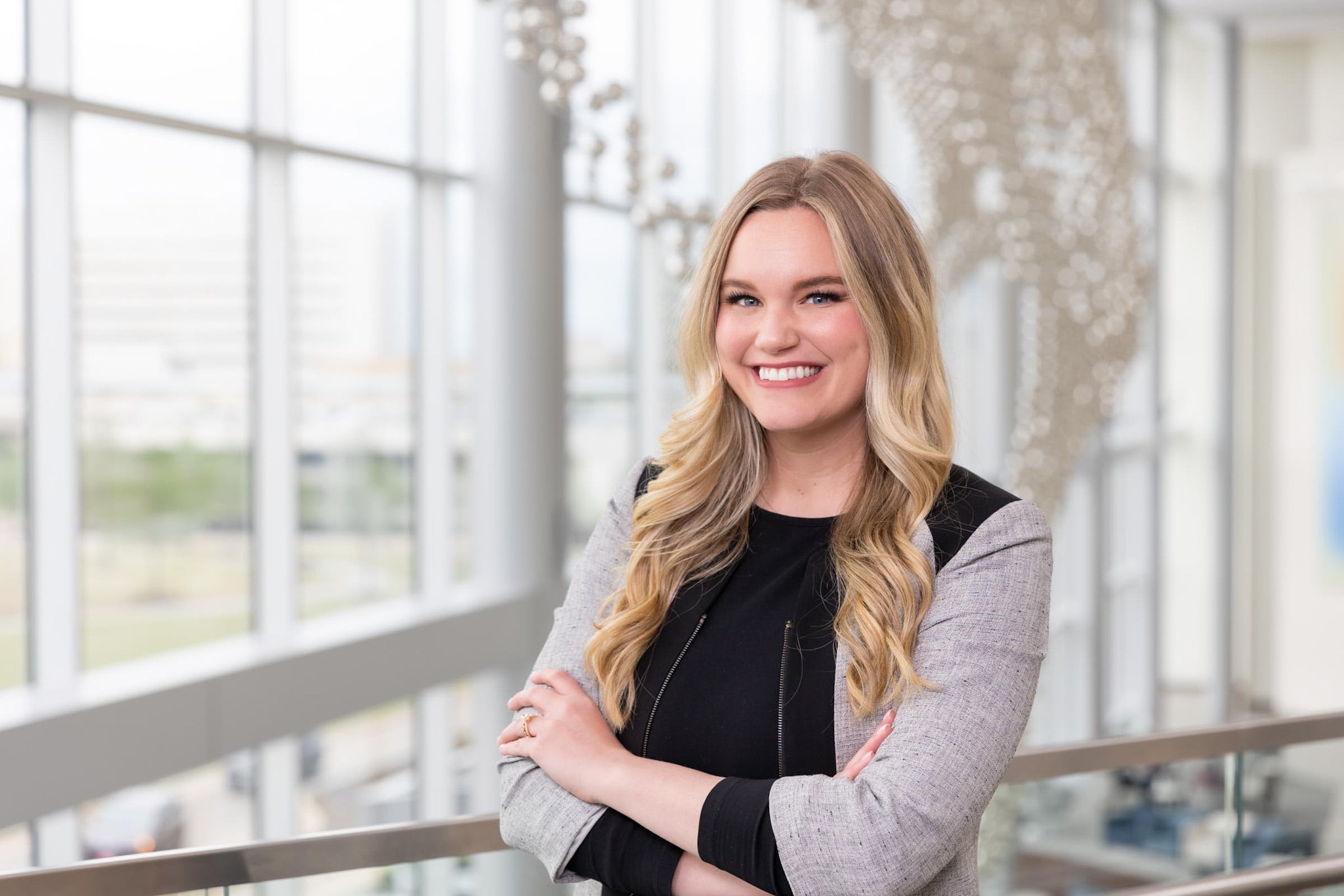 Avery Bottger smiling with arms folding in atrium with big windows. She is wearing a black and gray blazer." _languageinserted="true