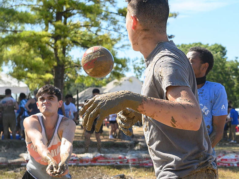 Students covered in mud playing volleyball at Oozeball