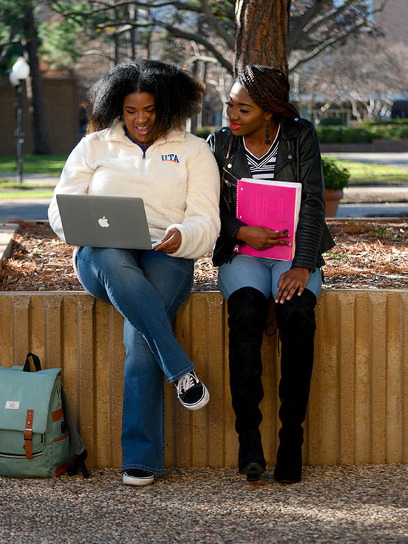 Students sitting on ledge looking at a computer