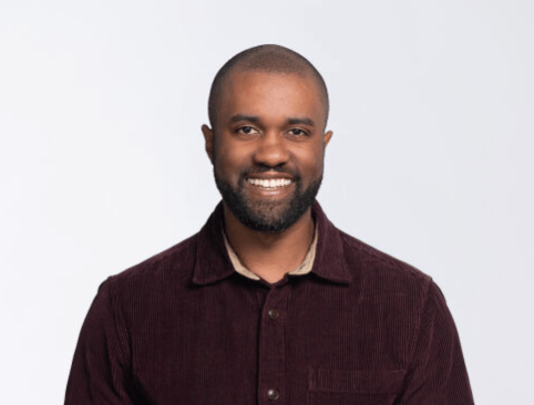 Gerrell Williams smiling at the camera wearing a dark button up in front of a plain backdrop