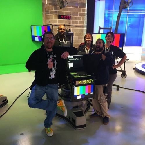 Omar and coworkers gathered around a teleprompter in a studio.