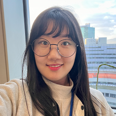 Bo Won Kim smiling with long hair, bangs, glasses, and a turtleneck.