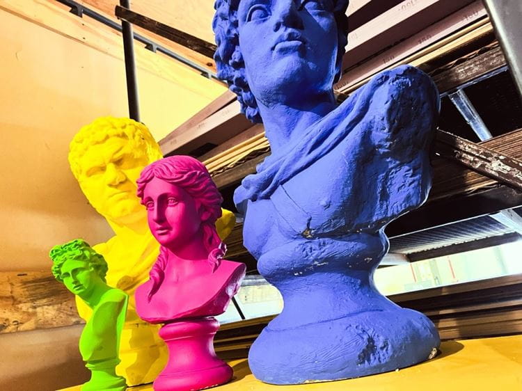 4 greek busts of varying sizes in bright colors that are positioned around campus