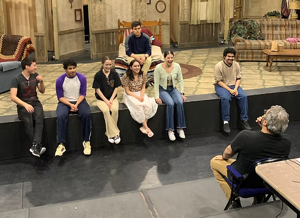 Playwright Octavio Solis speaks to a group of actors sitting on edge of stage.