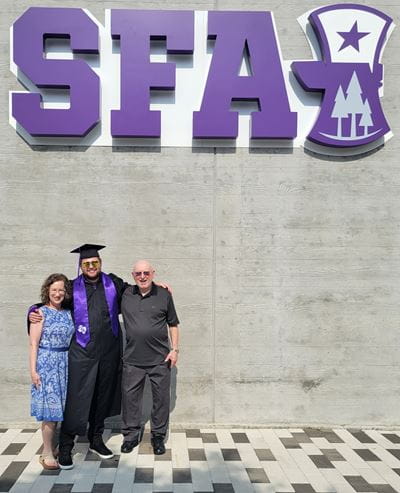 Photo of Catherine Hinton with her family at an Stefen F. Austin University graduation with large 'SFA' letters in the background.