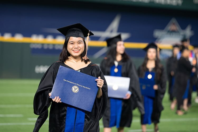 female UTA graduate holding her diploma at globe life field