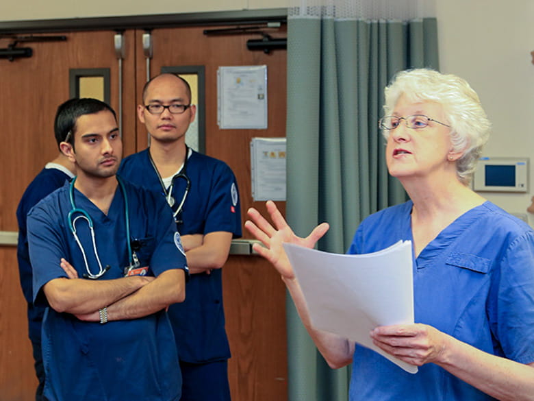 female instructor in scrubs speaking with male nursing students
