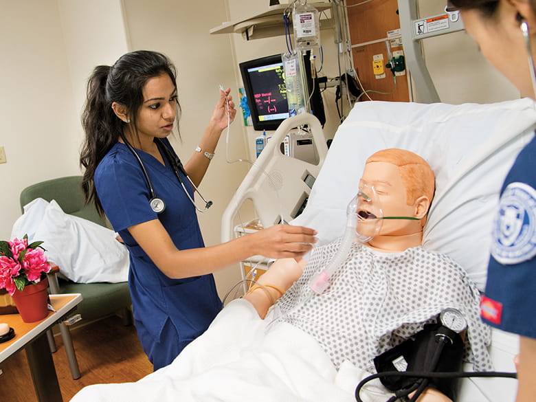 A student assists a simulated patient wearing an oxygen mask.