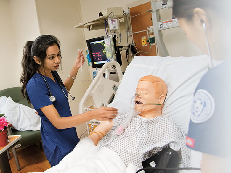 Two nursing students tend to a simulated patient wearing a blood pressure cuff. 
