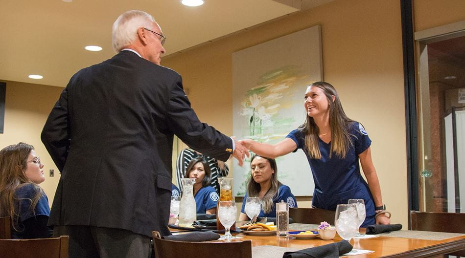 A donor shakes the hand of a nursing scholarship recipient at a formal dinner event. 