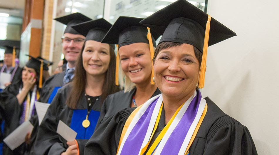A group of four students wearing cap and gowns prepare for a graduation ceremony.