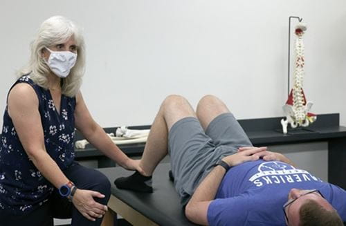 Cindy Trowbridge demonstrating athletic training technique on a male student reclined on a table