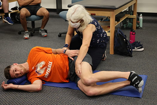 Dr. Cynthia Trowbridge instructs and adjusts athletic training student on a floor mat