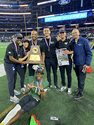 Chad Rodriguez posing with Head Athletic Trainer David Young at Desoto High School and other coaches on the field at Texas 6A State Football Championship 