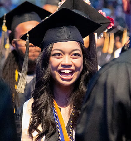 A student smiles as they walk down the aisle during a commencement ceremony. 