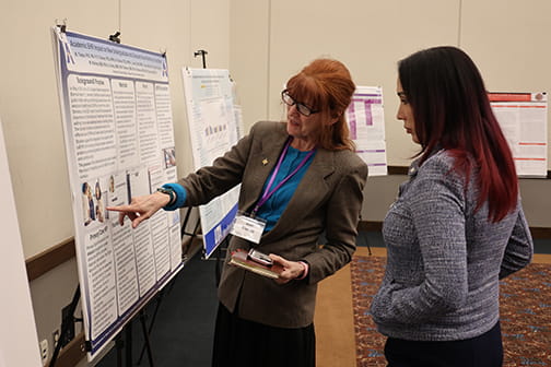 Dr. Mari Tietze pointing to poster and talking with student at symposium
