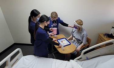 Simulated participant sitting at tray table while student nurses serve lunch