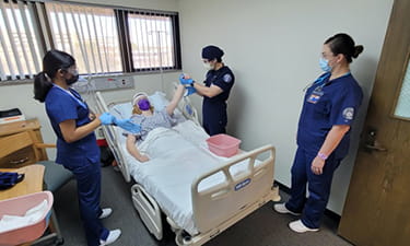 Simulated participant in bed  while nursing students check her