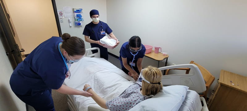 Simulated participant in bed  while nursing students check her