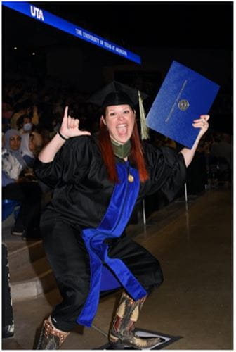 Claire Oliver at commencement cheering and doing the Mav hand sign