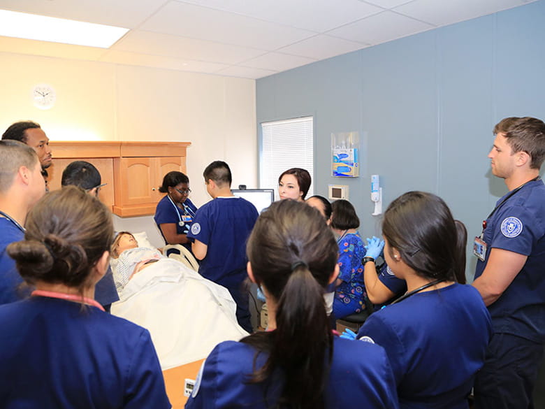 student nurses standing around simulation mannequin in the bed while being taught