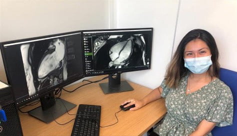 female student sitting along side of 2 computer monitors showing a project