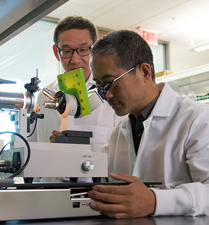 Two researchers in lab coats use a microscope to conduct an experiment