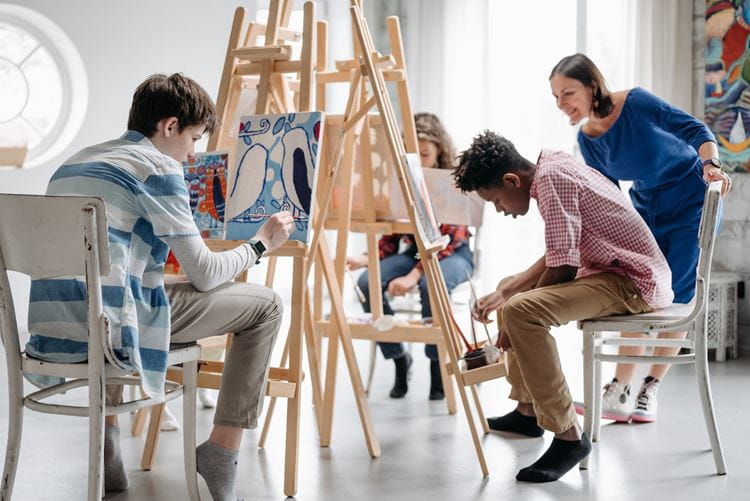 A classroom of students use easels to paint 