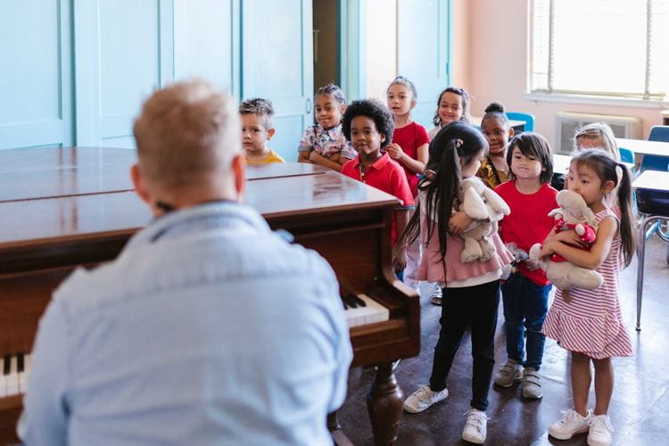 Teacher playing the piano in front of a group of young children 