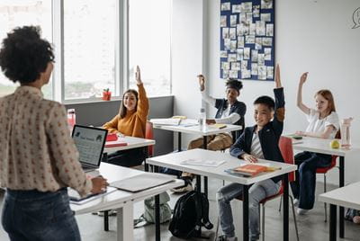 Middle school teacher with students raising hands in a classroom 