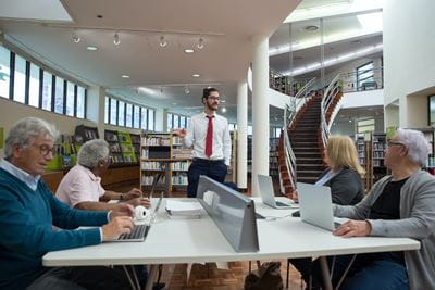 A teacher helps a classroom of senior citizens work on digital technology in a library class. 