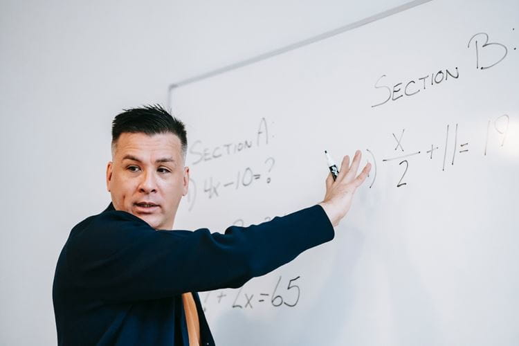 A teacher talks beside a whiteboard in a classroom