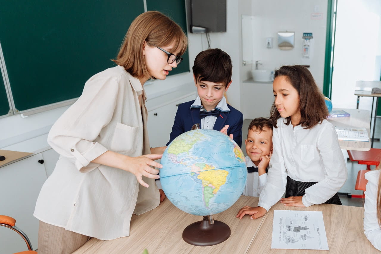 A teacher showing a country on a globe for a small group of students inside a classroom.