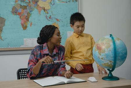 A teacher and a student looking at a globe in a classroom 