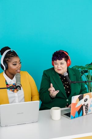 2 people sitting at a podcast table with lapts on the table