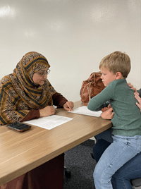 A lady wearing a hijab sitting and working with a child on an assignment